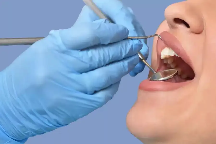 Zahnarzt mit blauen Handschuhen untersucht den offenen Mund eines Patienten mit einem Mundspiegel und einer Sonde vor blauem Hintergrund.